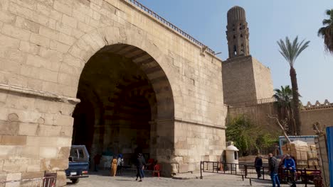 people and cars passing under bab al-futuh gate in city wall of cairo old city, egypt. handheld