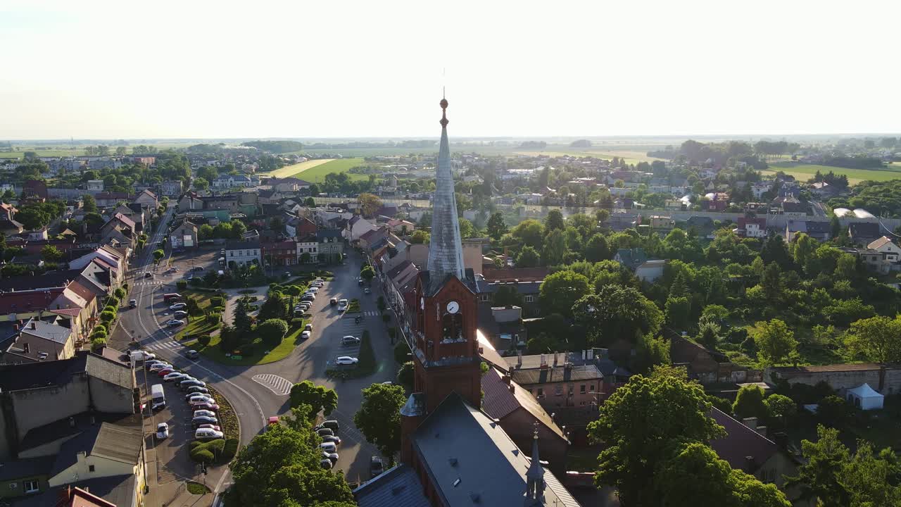 Evening sun illuminates Czempiń's iconic red church tower above lush countryside