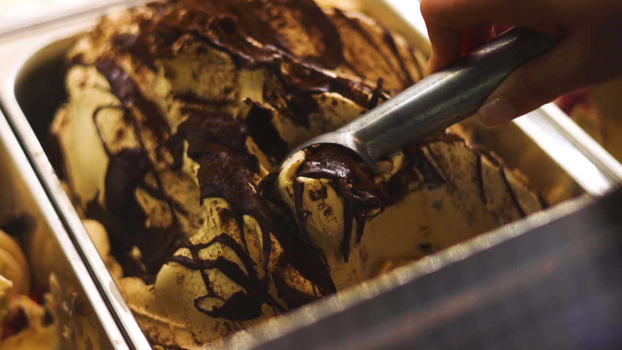 Mano femminile curata che preleva gelato al cioccolato e nocciola da una vaschetta di gelato