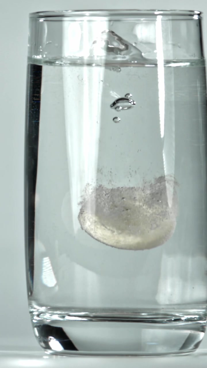 Compressa effervescente che si dissolve in un bicchiere d'acqua al rallentatore.