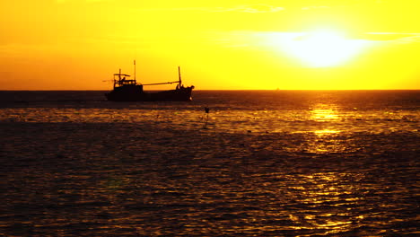 silhouette of fishing boat returning home during golden sunset time, static view