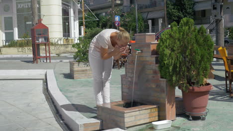 Junge-Frau-Wäscht-Ihr-Gesicht-Im-öffentlichen-Brunnen-Auf-Der-Straße-Im-Sommer-In-Piräus,-Griechenland