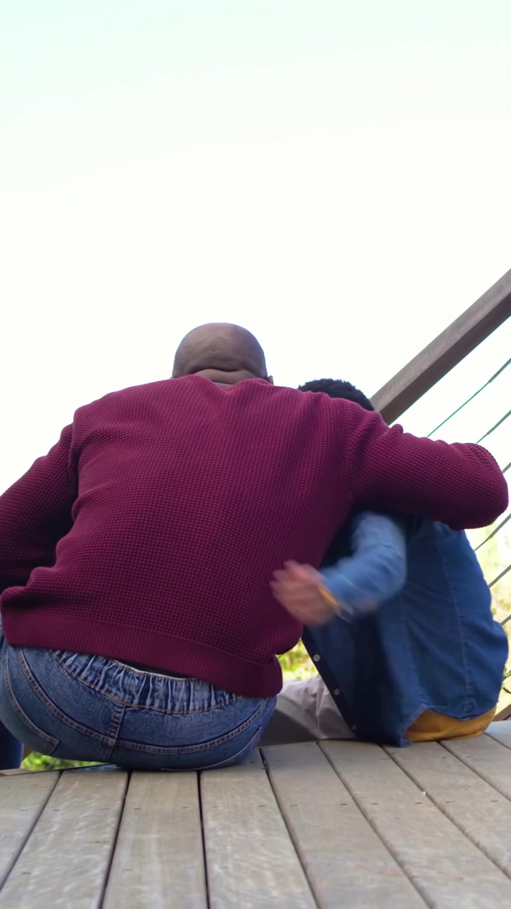 Video verticale: Un ragazzo appare, un uomo con maglione bordeaux si allunga, lo tira a sé, creando un legame sul ponte.