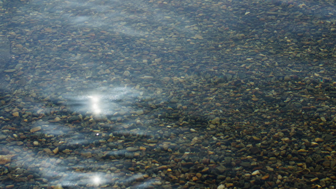 tiro estático de água cristalina com pequenas pedras abaixo com o sol refletindo