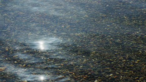 static shot of crystal clear water with small pebbles below with the sun reflecting