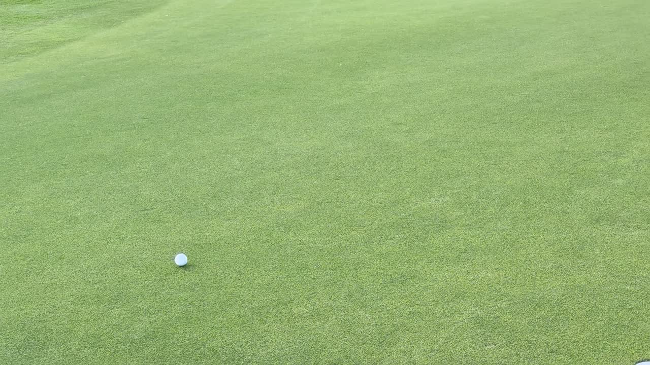 Una pallina da golf bianca rotola su un putting green verde lussureggiante verso una bandierina rossa.