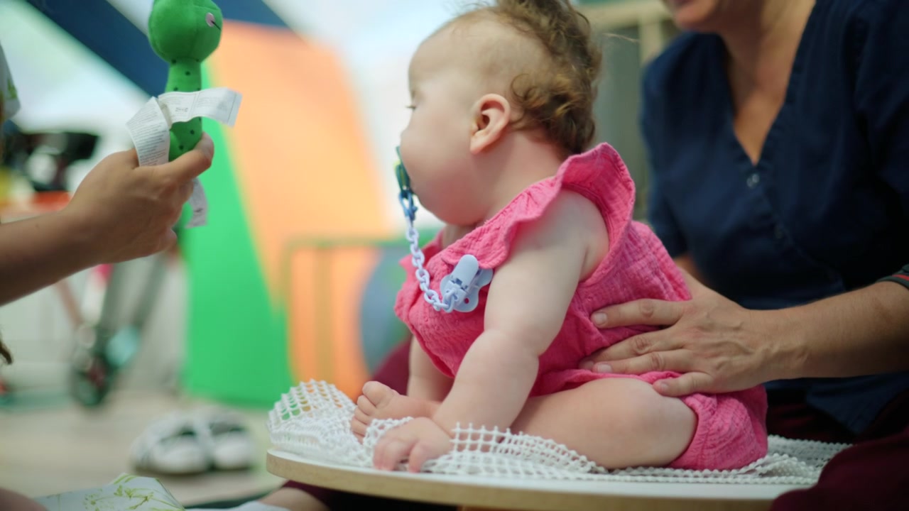 Baby girl sitting on a therapy disc, supported by a therapist during an early intervention physical development session