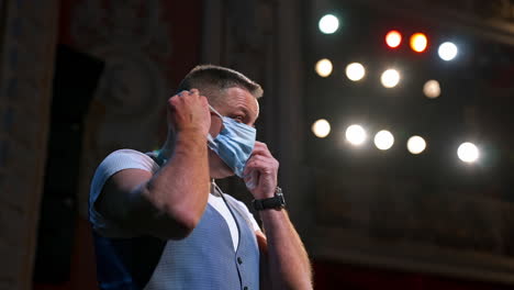 man on the theater stage. middle-aged man dressing on medical mask during coronavirus in spotlights. side view.