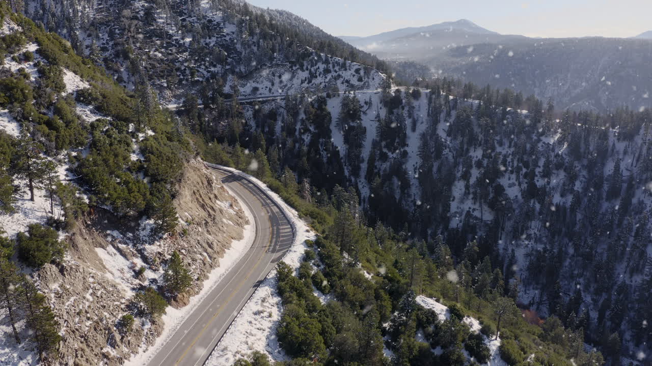toma aérea de un sinuoso camino de montaña en un paisaje invernal nevando