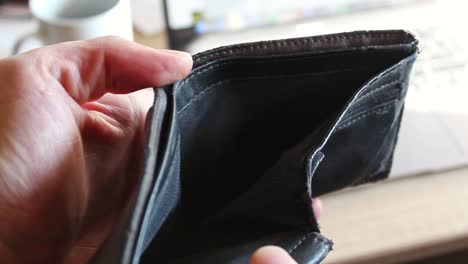 hands opening a brown leather wallet with no money inside