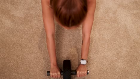a woman exercises with an abdominal wheel on a carpeted floor, focusing on core strength in a well-lit home setting