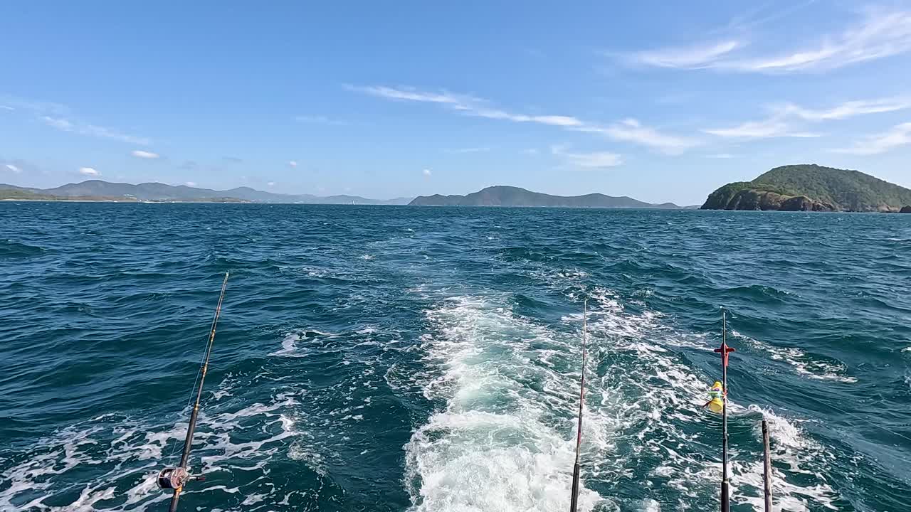 A fishing boat navigates the clear, blue waters near Phuket, Thailand, under bright daylight with visible fishing rods