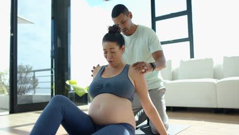 helping pregnant woman with exercise, man supporting her on yoga mat indoors