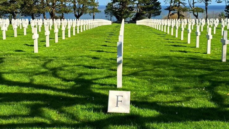 Rækker af hvide kors på den amerikanske kirkegård i Normandiet, Frankrig, med udsigt over havet i et højtideligt mindelandskab fra Anden Verdenskrig under klart forårslys.