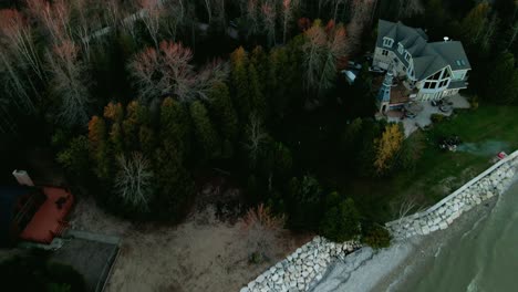 Aerial-zoom-on-large-mansion,-lush-trees,-roads,-and-coastal-views-in-residential-Wisconsin-on-the-water