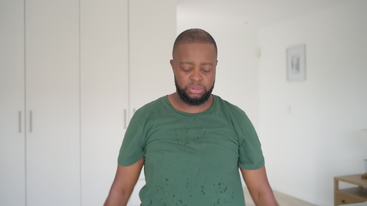 Homem afro-americano de camiseta verde alongando-se no quarto, preparando-se para o treino de bicicleta ergométrica.