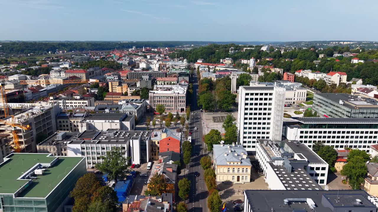 Aerial view of central Kaunas, Lithuania, showcasing a mix of modern and historic buildings, green spaces, and bustling urban development under clear summer skies