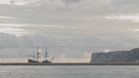 16th century galleon andalucia replica ship arriving at port in a beautiful cloudy day at sunrise behind a breakwater with mountain in the background