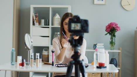 cámara grabando un video de una joven bloguera de belleza hablando de brillos de labios y diciendo cuál es mejor