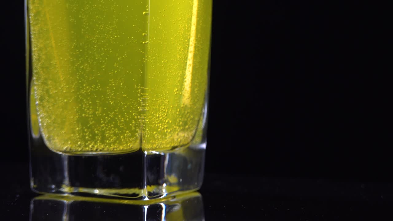 cerca de la tableta de vitamina c disuelta en un vaso de agua mineral fresca en un fondo oscuro. tiro macro de líquido burbujeante amarillo con bolas de oxígeno