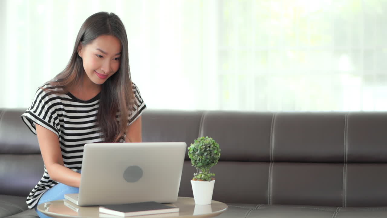 A young attractive Asian woman working on her laptop sitting on her coffee table