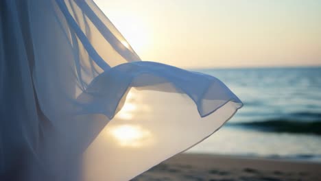 a flowing fabric dances in the gentle breeze near the ocean at sunset, capturing the ethereal beauty and serene moment against the fading light of day