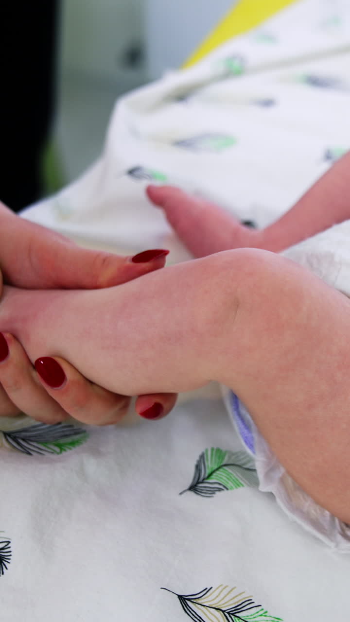 Doctor is checking the toddler's development. Female pediatrician turning baby's foot and checks the leg. Close up. Vertical video
