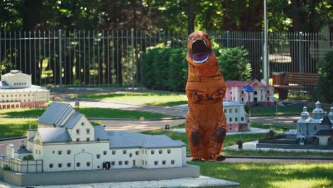 cartoon animation. dragon costume in small city. person wearing blow-up animal suit walking among beautiful handmade architecture in the park.