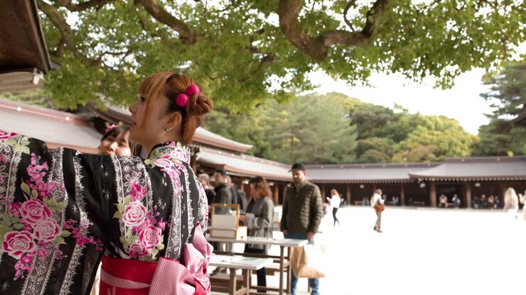 Una donna in un kimono floreale tradizionale esamina le tavolette votive in un luminoso santuario shintoista