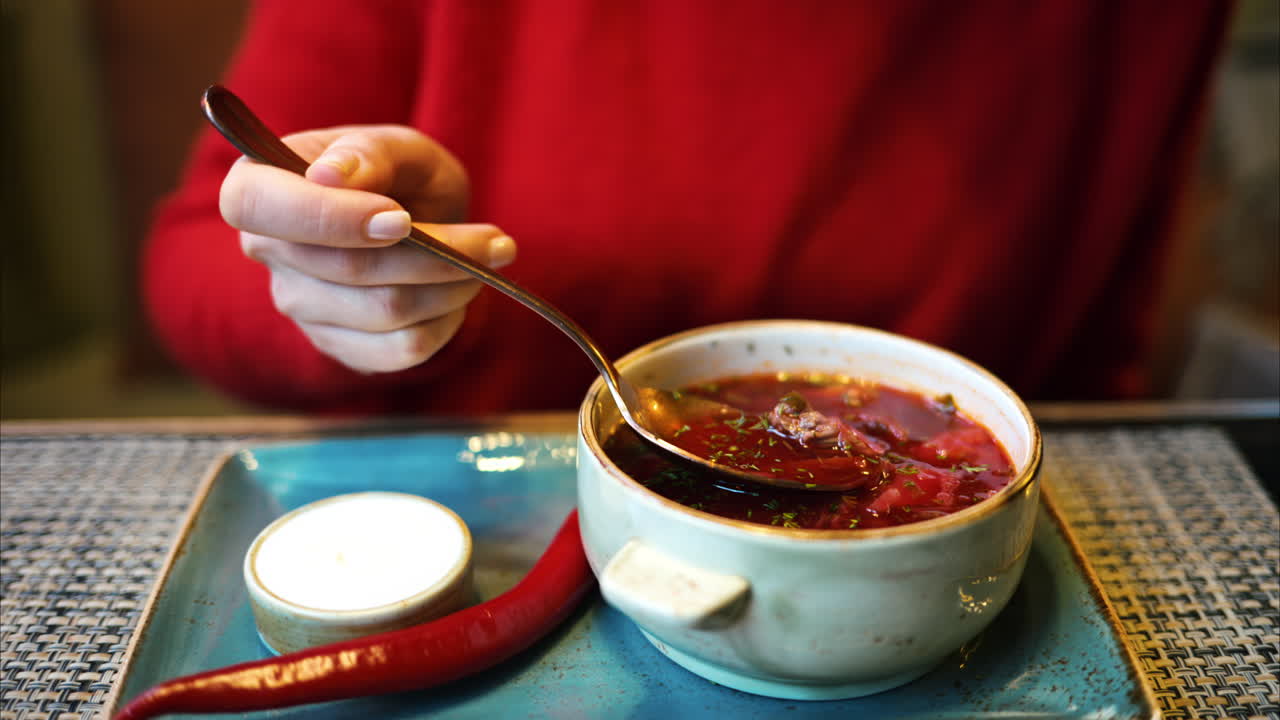 Woman eating red borscht vegetable soup in restaurant. Sour cream and red hot pepper