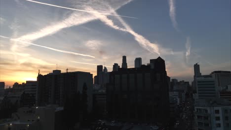 aerial ascending shot to reveal silhouetted downtown los angeles with epic orange golden sunset skies with contrails