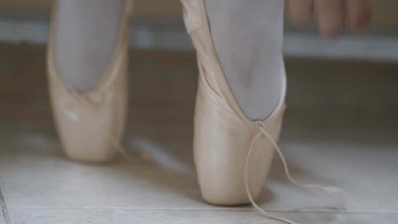 primer plano de los pies de la bailarina de ballet mientras ata los cordones de su zapatilla de ballet