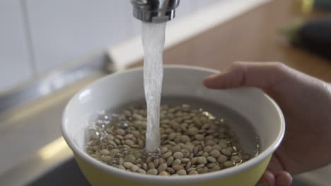 preparando ingredientes para cocinar, remojando las lentejas en un tazón, abriendo un grifo, corriendo agua en la cocina