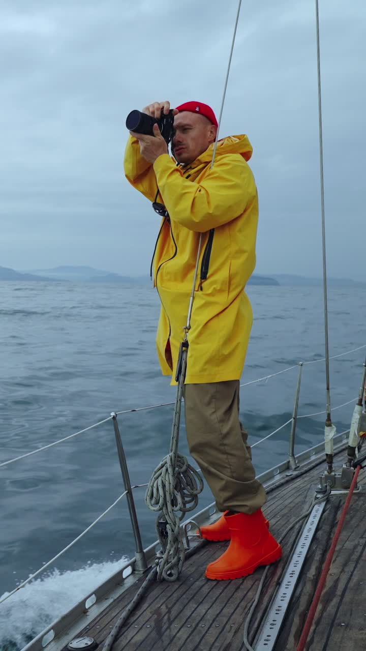 Homme en imperméable jaune prenant des photos sur un voilier en mer