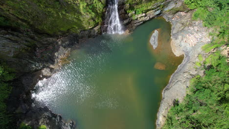 Aufsteigende-Drohnenaufnahme-Eines-Natürlichen-Sees-Im-Dschungel-Mit-Wasserfall-An-Einem-Sonnigen-Tag