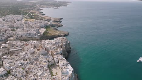 wide aerial side to side shot showing the town of polignano a mare and the cliffs and sea that it sits next to in italy