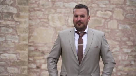 Groom-straightens-his-suit,-slow-motion-with-a-brick-wall-background