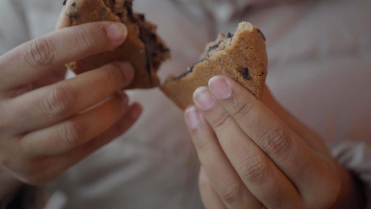 cerca de las manos de una persona rompiendo una galleta de chispas de chocolate revelando un relleno de chocolate