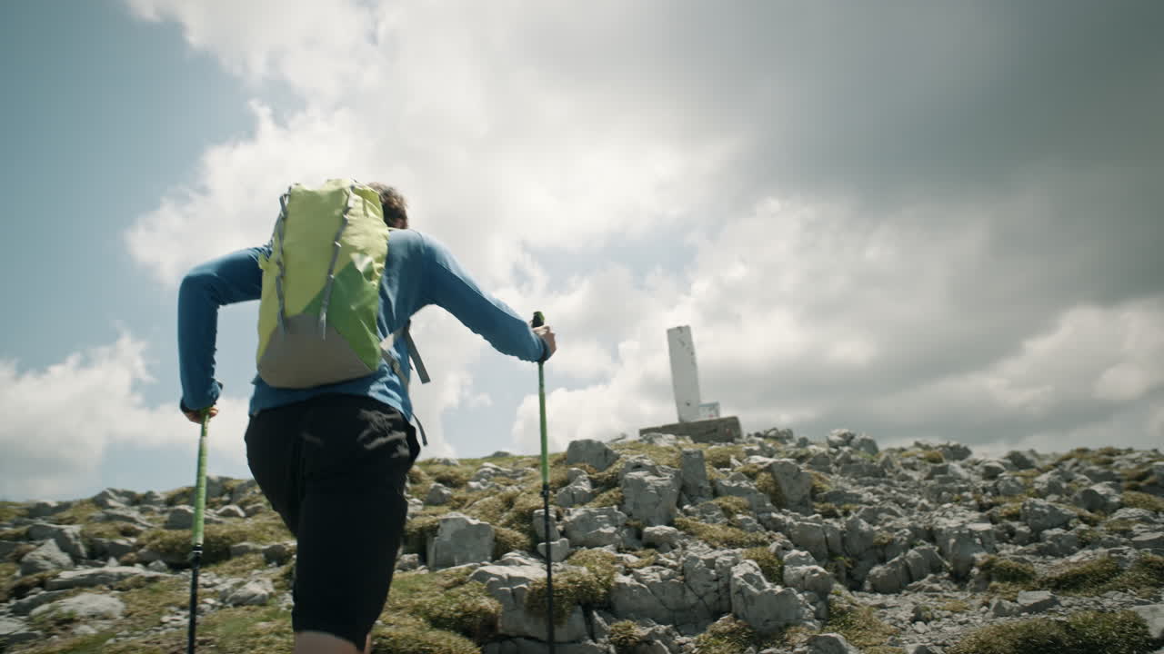 seguimiento de cámara detrás de un excursionista con una mochila verde caminando con bastones de senderismo hacia el monumento rocoso