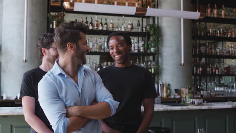 portrait of male owner of restaurant bar with team of male waiting staff standing by counter