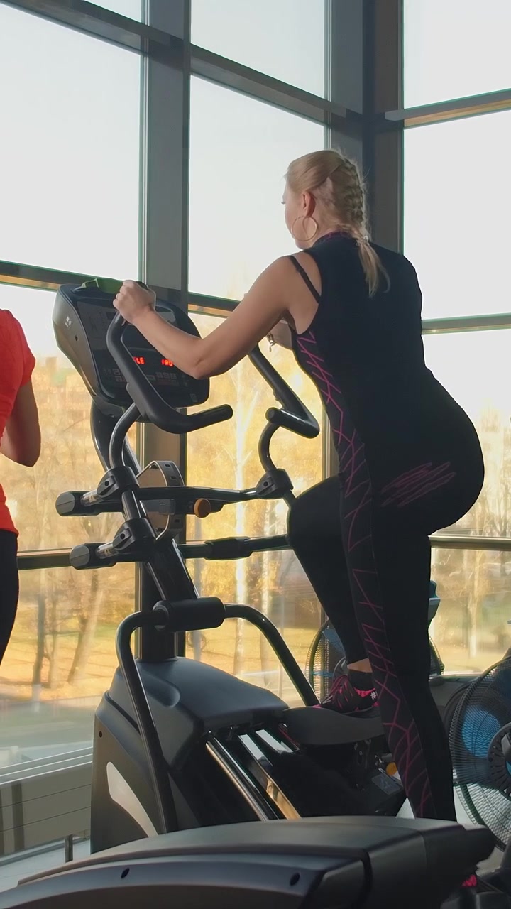 Two Women Exercising on Elliptical Machines in a Gym