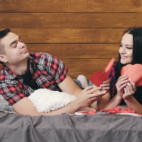 man holding three paper hearts gives them to his girlfriend and they are kissing passionately on bed. happy lovely couple lying in bed flirting to one another at home. close-up