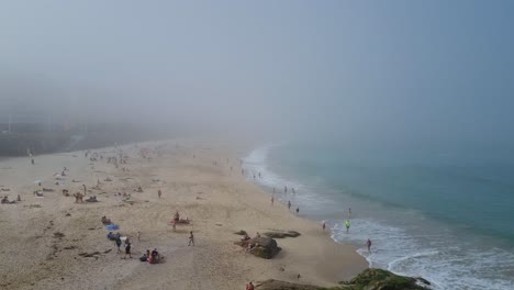 view on busy beach of central a coruna, spain on a mystical foggy day, mist covering the horizon and atlantic waves hitting the shore