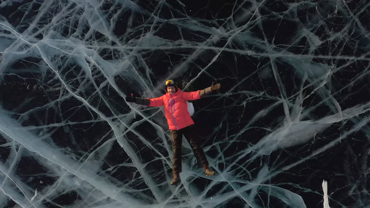 한 남자가 겨울에 얼음 위에 누워서 팔과 다리를 으로 펼쳐서 물에 떠 있는 척하고 천사를 묘사합니다.