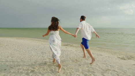 Joven-Pareja-De-Enamorados-En-Ropa-Ligera-Sin-Preocupaciones-Corriendo-En-Una-Playa-Tropical-Limpia