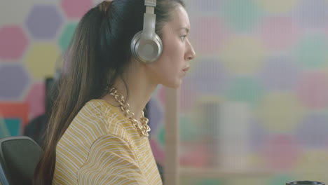 close up beautiful young asian woman student using computer brainstorming working on creative project enjoying study in colorful modern office listening to music wearing headphones