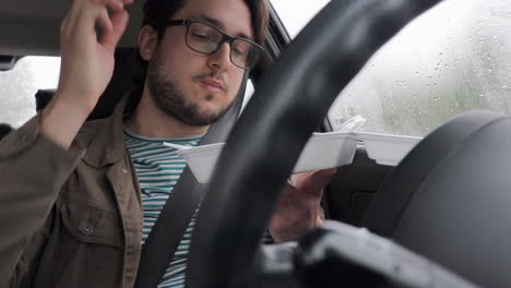 el joven conductor come comida para llevar en su auto - día lluvioso