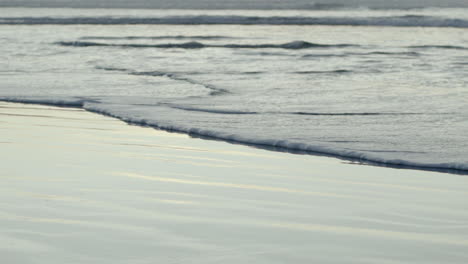 Close-up-of-foamy-ocean-wave-slowly-drifting-on-the-wet-sand-with-reflections