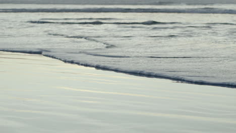 Nahaufnahme-Einer-Schäumenden-Ozeanwelle,-Die-Langsam-Auf-Dem-Nassen-Sand-Mit-Reflexionen-Driftet