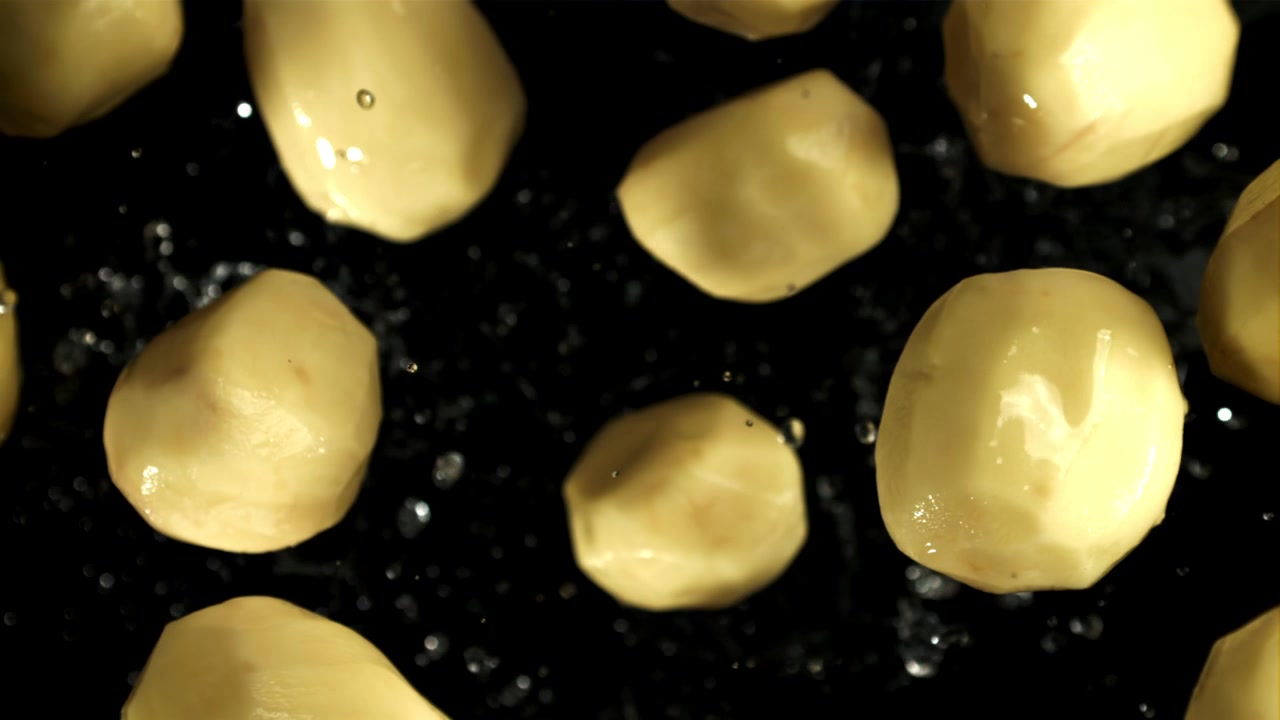 Patate fresche pelate che cadono con gocce d'acqua al rallentatore